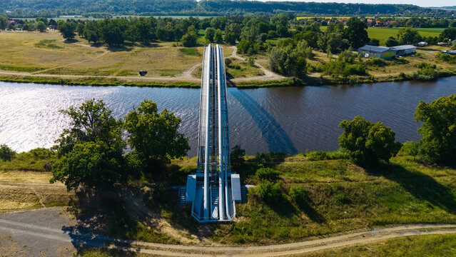Aerial view of a gas pipeline bridge crossing a wide river surrounded by lush green trees and fields Nova Ves, Central Bohemian Region, Czechia.