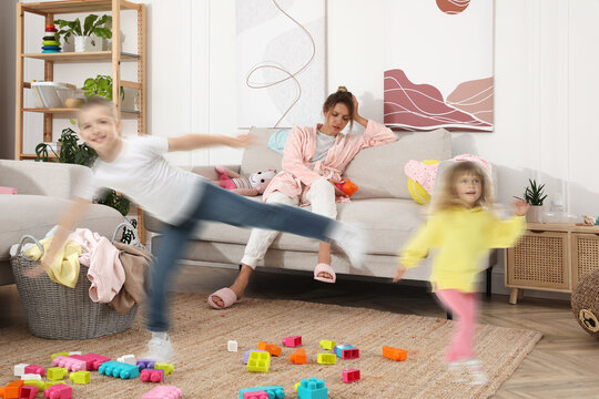Family with hyperactive children. Tired mother sitting on sofa while her kids having fun