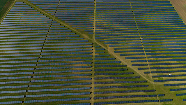 Aerial view of Veprek Solar Park with rows of photovoltaic panels on green fields under bright sunlight in Nova Ves u Melnika, Central Bohemian Region, Czechia.
