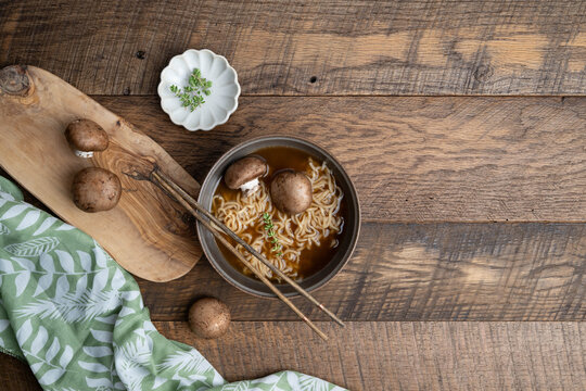 Hot noodle pho soup with whole, baby portabella mushrooms, noodles and thyme on a wooden table with green and white napkin towel and chopsticks