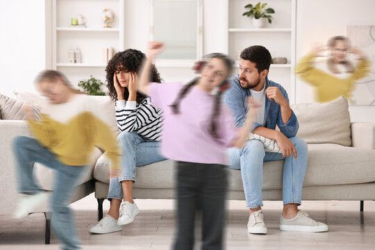 Family with hyperactive children. Kids having fun while tired parents sitting on sofa