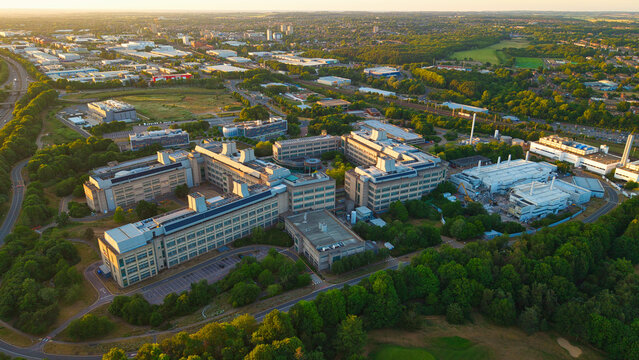 Aerial view of the GSK Stevenage research and development campus with modern laboratory buildings surrounded by lush green trees and urban landscape in Stevenage, England, United Kingdom.