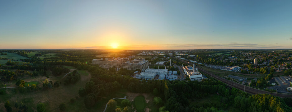Aerial view of the GSK Stevenage campus at sunset with industrial buildings, railway tracks, and surrounding green landscape in Stevenage, England, United Kingdom.