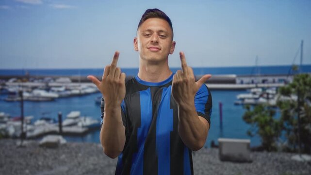 Man shows middle finger with bare hands on street near marina boats and pier; defiance rivalry fan team.