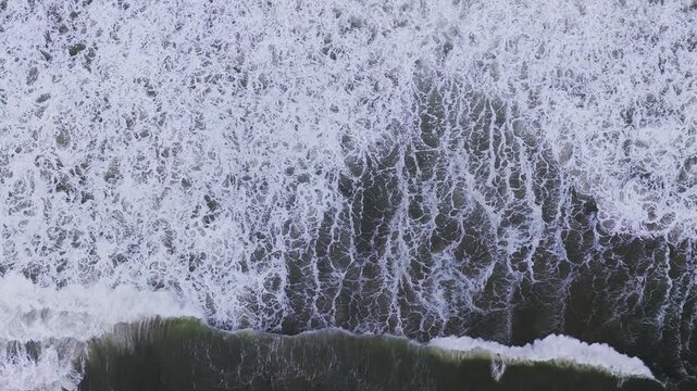 Aerial top down view of Atlantic surf near Cape Town shows breaking waves, white foam, and darker rip currents under overcast daylight, forming parallel bands and motion.