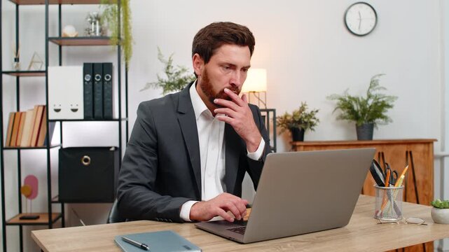 Middle-aged businessman at home office reads pay cut email on laptop and sighs after bad news sadly. Freelancer guy at table frowns thinking about salary cut and next steps for bills budget and rent.