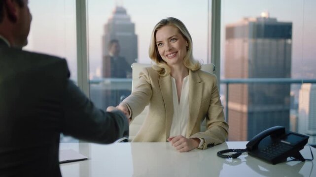 Blonde businesswoman in beige blazer shaking hands with colleague in modern office interior