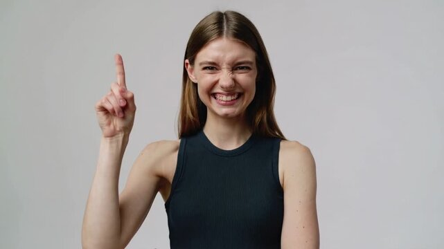 Young woman in dark grey tank top thinking and having an idea against grey background eye level