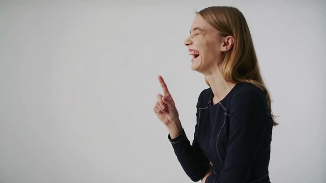 Young woman in dark blue dress thinking and pointing finger against white background medium shot