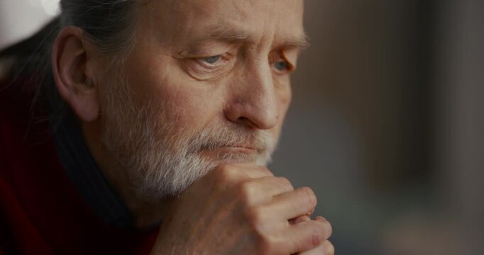 Thoughtful elderly man with gray beard resting hand on chin