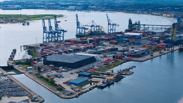 Aerial view of the Port of Tilbury with rows of shipping containers and tall blue gantry cranes along the River Thames in Tilbury, England, United Kingdom.