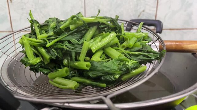 Close Up View of Freshly Boiled Green Vegetables Steaming on Wire Skimmer Over Kitchen Wok