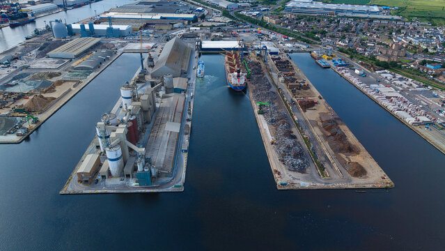 Aerial view of the Port of Tilbury featuring industrial docks, cargo ships, and large storage silos under a clear sky in Tilbury, England, United Kingdom.