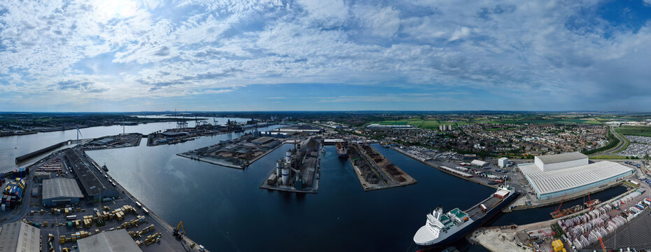 Aerial view of the Port of Tilbury with cargo ships, industrial docks, and warehouses along the River Thames under a bright cloudy sky Tilbury, England, United Kingdom.