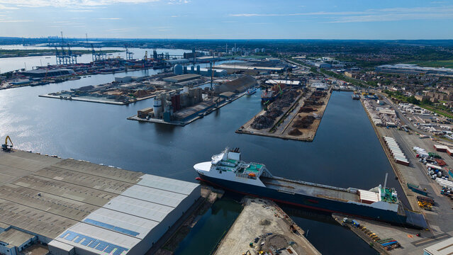 Aerial view of Port of Tilbury featuring a large cargo ship docked at the industrial terminal with warehouses and cranes under a clear blue sky Tilbury, England, United Kingdom.