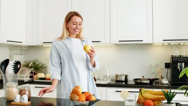 Middle-aged woman biting fresh apple at home kitchen table enjoying healthy snack for vitamins and diet. Young girl choosing fruit instead of sweets supporting clean eating and wellness daily routine.