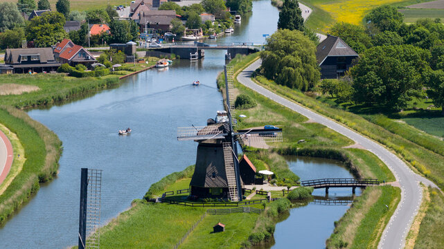 Aerial view of the historic Strijkmolen K windmill standing beside a calm canal with boats and lush green banks in Oterleek, Noord-Holland, Netherlands.