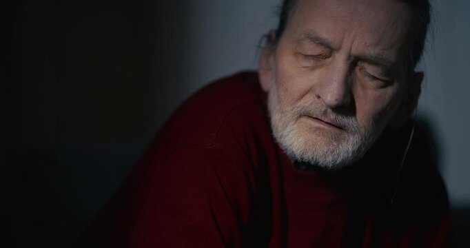 Serious elderly man in dark sweater with dramatic indoor lighting