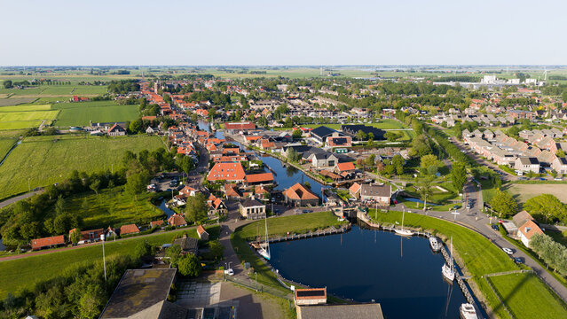 Aerial view of the town featuring a canal with boats and traditional red-roofed houses under a clear sky in Workum, Friesland, Netherlands.