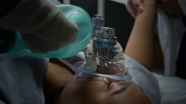 Black woman lying in hospital bed with medical professional administering oxygen using Ambu bag mask. Footage is perfect for healthcare training and clinical promos, close up