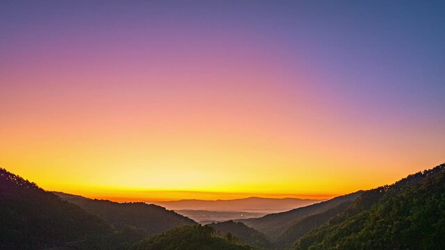 A stunning aerial hyper lapse captures the first light of sunrise spreading across a peaceful mountain valley beneath a colorful sky gradient. Scenic Aerial View of Mountains and Sunrise