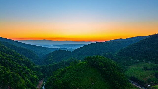 Aerial Hyper lapse Stunning Morning Light Over a Tropical Valley. Golden and pastel hues illuminate the horizon as the sun rises over rolling forested hills, creating a breathtaking natural panorama