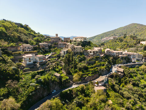 Aerial view of the historic hillside village featuring stone houses, winding roads, and lush green Mediterranean vegetation under a clear sky Savoca, Sicily, Italy.