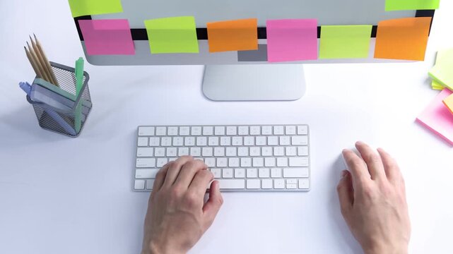 Man typing on computer keyboard and colorful sticky notes at white table, above view. Multitasking, deadline and rush at work