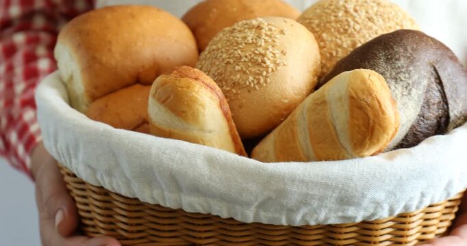 Woman holding wicker basket with different types of bread indoors, closeup. Camera moving out