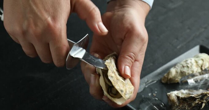 Woman opening oyster with knife at black table, closeup