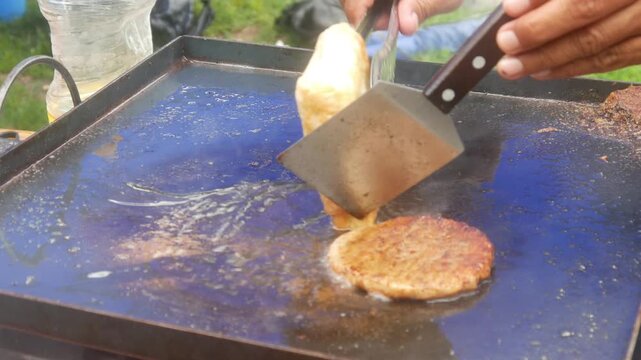a person's hands cooking square shaped egg martabak and burger patty meat on a hot flat pan
