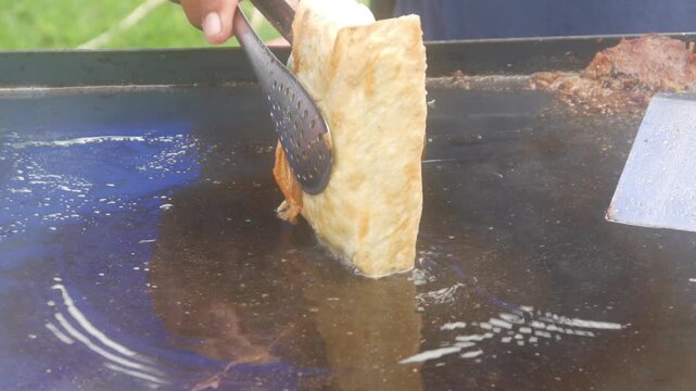 a person's hands cooking square shaped egg martabak and burger patty meat on a hot flat pan
