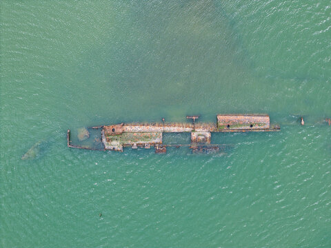 Aerial view of the rusted remains of a German Submarine shipwreck partially submerged in the green waters of the estuary River Medway, Kent, United Kingdom.