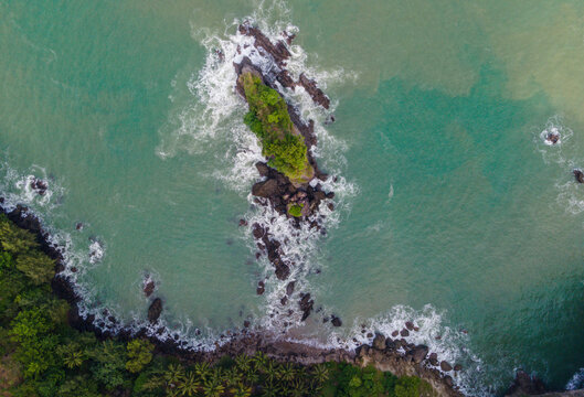 Aerial view of the iconic Karang Agung rock formation surrounded by turquoise sea water and crashing waves near the coastline Ayah, Central Java, Indonesia.