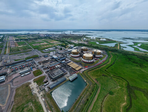 Aerial view of the Grain LNG terminal with large storage tanks and industrial infrastructure surrounded by green fields and waterways in Wallend, England, United Kingdom.