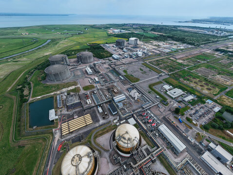 Aerial view of the Grain LNG terminal featuring large storage tanks and industrial infrastructure surrounded by green fields near the coast in Wallend, England, United Kingdom.
