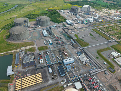 Aerial view of Grain LNG terminal featuring large storage tanks, industrial infrastructure, and complex pipeline networks under a clear sky in Wallend, England, United Kingdom.