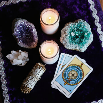 Collection of crystals candles, tarot cards on purple cloth for spiritual ritual. Amethyst geode quartz cluster, blue green druzy with sage bundle for healing energy. Mystical altar setup for