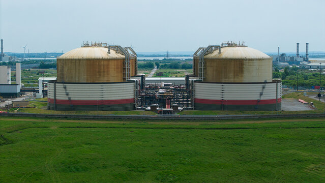 Aerial view of the Grain LNG storage tanks featuring large cylindrical structures and industrial infrastructure surrounded by green fields in Wallend, England, United Kingdom.