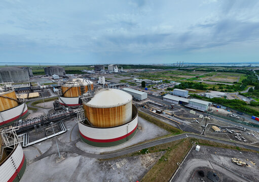 Aerial view of Grain LNG terminal featuring large storage tanks and industrial infrastructure under a cloudy sky in Wallend, England, United Kingdom.