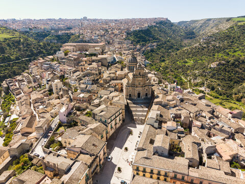 Aerial view of the historic center of Ragusa Ibla with the Cathedral of San Giorgio surrounded by ancient stone buildings and lush green valleys Ragusa, Sicily, Italy.