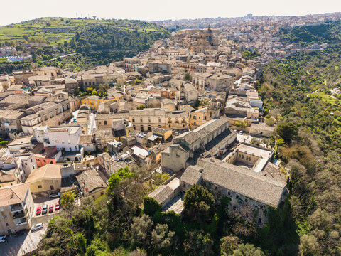 Aerial view of the historic baroque architecture and stone buildings of Ragusa Ibla with the Duomo di San Giorgio and green hills Ragusa, Sicily, Italy.