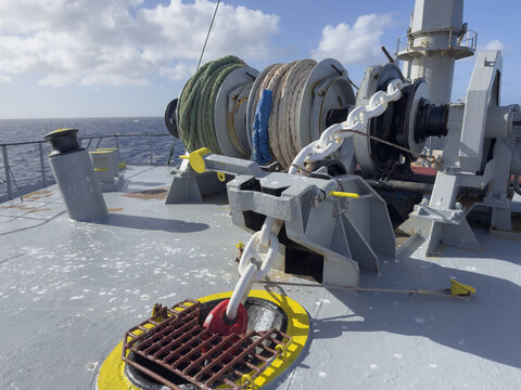 Forecastle deck of a cargo ship with complete mooring and anchoring system. Anchor chain led through chain stopper to windlass gypsy wheel. Mooring winch with professionally stowed mooring lines 