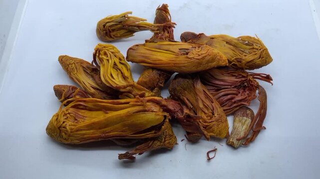 pile of dried Rampatri (Wild Mace) pieces isolated on a clean white background. The image showcases the intricate, reticulated, and lacy texture of these orange-brown whole spices. 