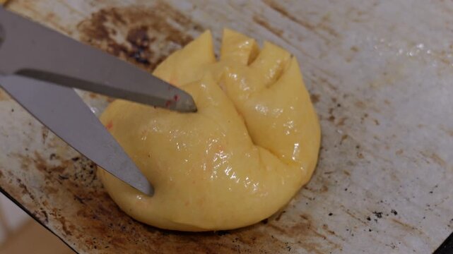 Scissors score a decorative star pattern on a single praline brioche ball