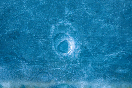 Aerial view of the frozen surface of Elk Lake featuring intricate ice cracks and a circular hole in the deep blue ice Elk, Warmian-Masurian Voivodeship, Poland.