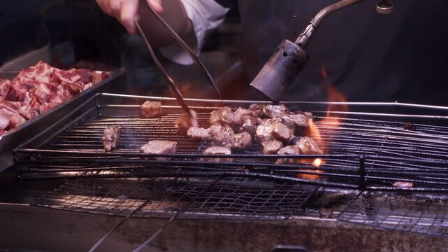 Close up of a the hands of a man cooking chopped beef with a blow torch to sell as street food at a night market in Taiwan.