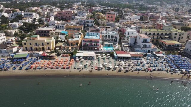 Aerial view of colorful beach umbrellas and coastal buildings along the waterfront in the town of Ischia, Campania, Italy.