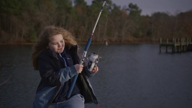 Kid fishing by calm water. Child enjoying fishing hobby. Kid angler near river. Child fishing during autumn day. Kid reeling fishing reel.