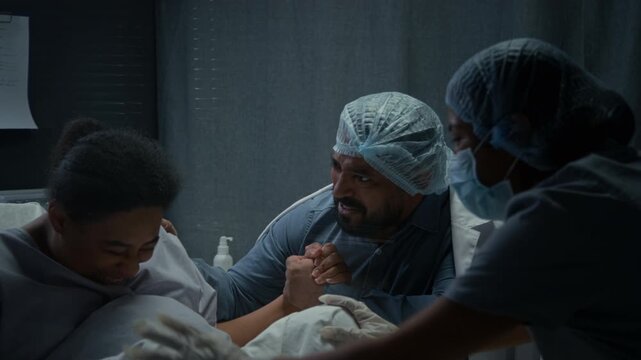 Black pregnant woman giving birth in hospital bed while husband holds her hand and doctors assist. Clip is perfect for maternity ward and childbirth education marketing